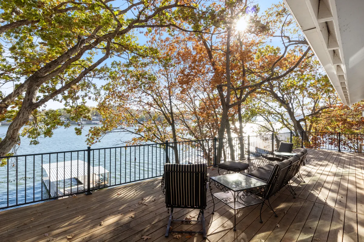 A wooden deck stretches toward the lake, flanked by autumn trees and offering both seating and open spaces for relaxation or gatherings. The lake shimmers beyond, illustrating the delight of sunrise or starlit evenings.