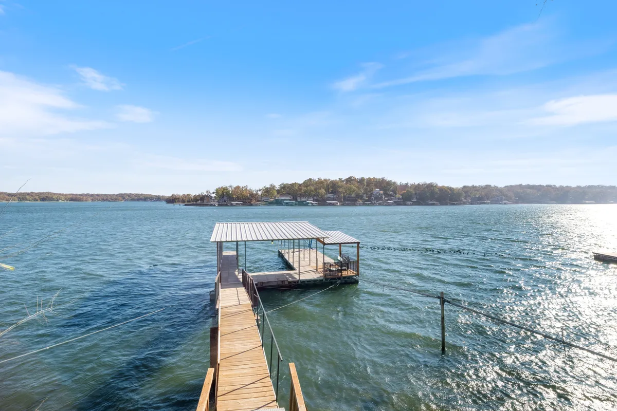 A wooden dock stretches over calm lake waters, with a boathouse nearby. The space offers serene views of the water and is ideal for fishing, boating, or simply relaxing by the shore. The dock appears spacious and well-kept, hinting at private access and relaxation options.