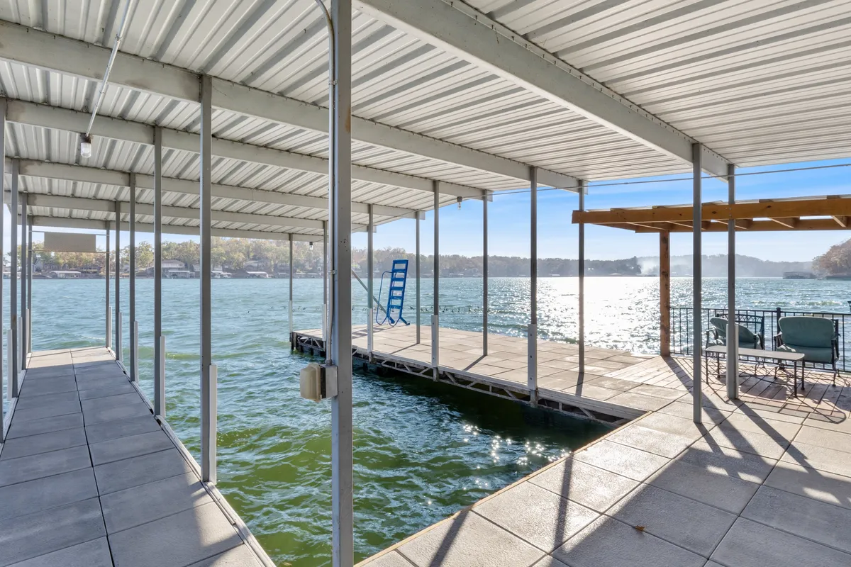 A peaceful scene featuring a dock with a seating area overlooking the gentle waters and the surrounding landscape. The dock is inviting for activities like fishing, relaxing, or watching boats drift by.