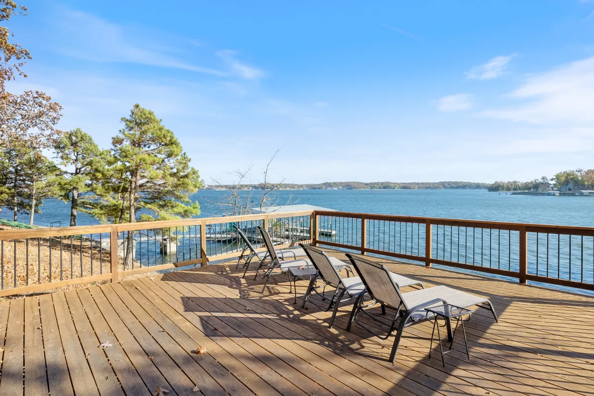 A wooden deck furnished with comfortable deck chairs, surrounded by trees and overlooking the tranquil lake. The wooden railing frames a sweeping view of the water, capturing the play of light at sunset and inviting moments of relaxation, reading, or conversation.