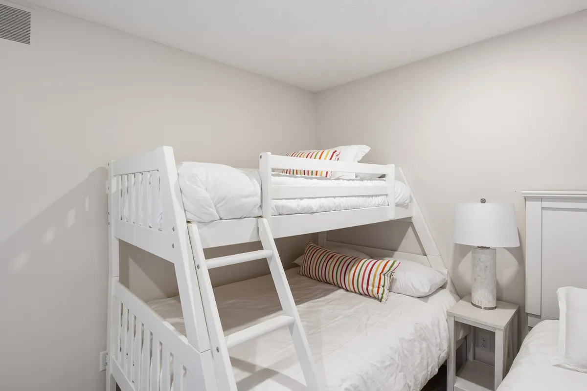 A playful, inviting space with a bunk bed dressed in striped pillows and a warm table lamp, suggesting an area suited for older kids, teens, or adventurous adults. The setup evokes sleepovers, bedtime stories, and the fun of shared adventures—perfect for a loft nook accessed by ladder.