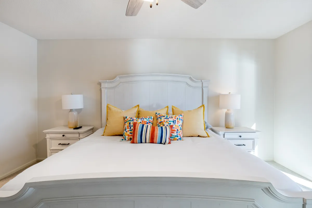 A comfortable bedroom sanctuary with a cozy bed adorned with decorative pillows, soft bedside lighting, and a ceiling fan overhead, inviting restful nights or quiet moments spent reading in bed. The mood is calm and welcoming, perfect for unwinding after a day by the lake.