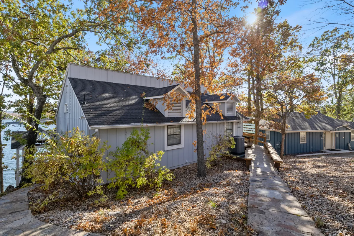 The house sits amongst mature trees, with a pathway leading directly to the water. The setting suggests easy access to outdoor activities and evenings around a fire pit, all within a welcoming, natural environment.