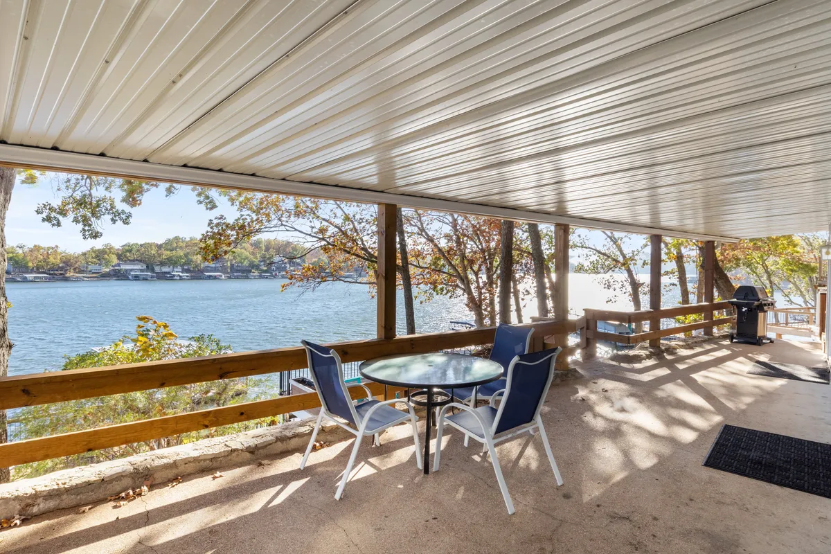 An outdoor dining table with chairs set on a deck that offers an unobstructed view of the lake. A grill stands nearby, suggesting alfresco meals with friends or family, while the calm water and treetops create a serene backdrop.