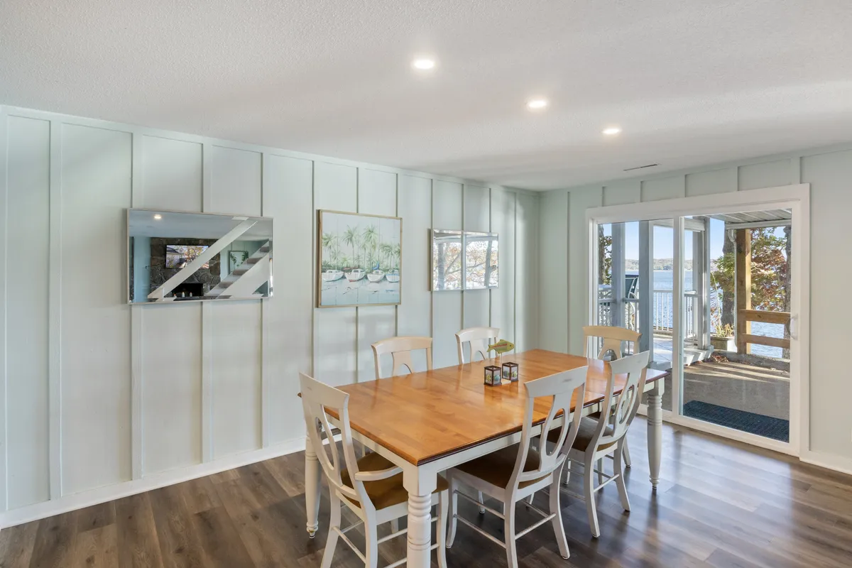 A spacious dining table sits near large windows that look out onto the outdoor area, with artwork adorning the walls and plenty of space for entertaining. The table is ready for family meals or holiday celebrations, with sunset light streaming in.