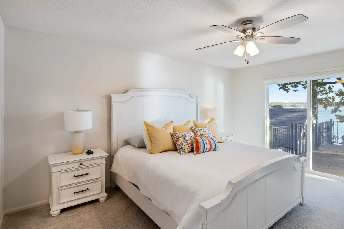 A cozy bedroom featuring a bed with vibrant pillows, a nightstand with a lamp for bedtime reading, and a large window that invites in calming natural light and beautiful outdoor scenery. The space feels peaceful and inviting, ideal for relaxation and restorative sleep.