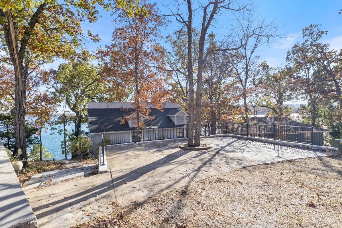 A peaceful patio area shaded by a large tree, with a clear lake view in the background. The space is perfect for small gatherings or quiet outdoor reflection, surrounded by natural beauty.