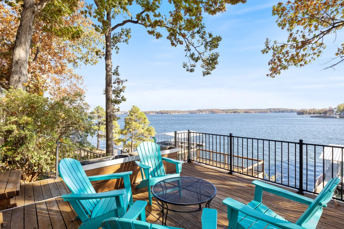 A peaceful wooden deck shaded by a tree canopy with Adirondack chairs facing the lake. The inviting setup encourages relaxation, socializing, and enjoying sunset views over the water.