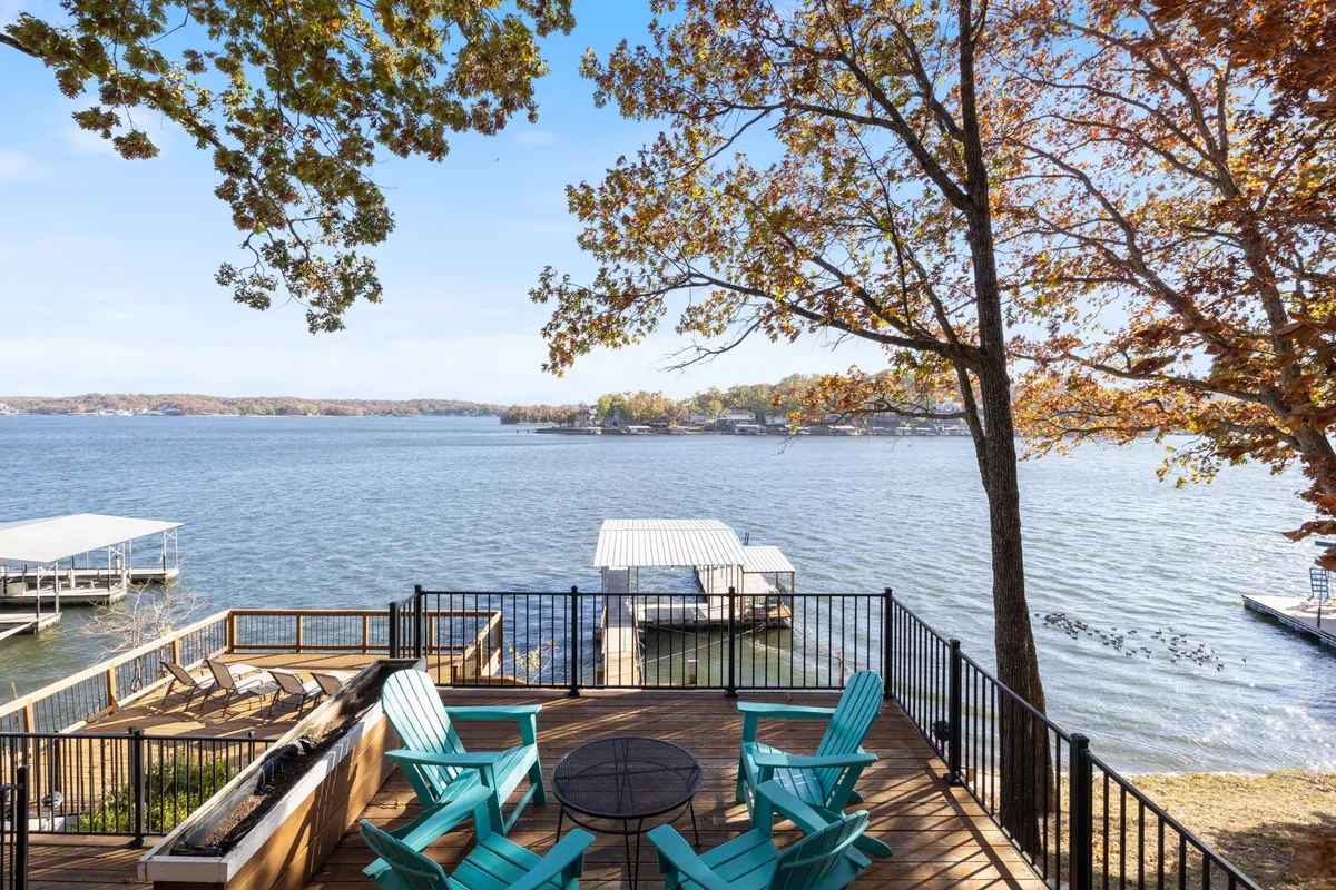 A peaceful lakefront scene featuring a private dock, classic Adirondack chairs, and brilliant autumn foliage. The dock extends into calm water, inviting fishing, swimming, or launching kayaks and paddleboards for adventure.