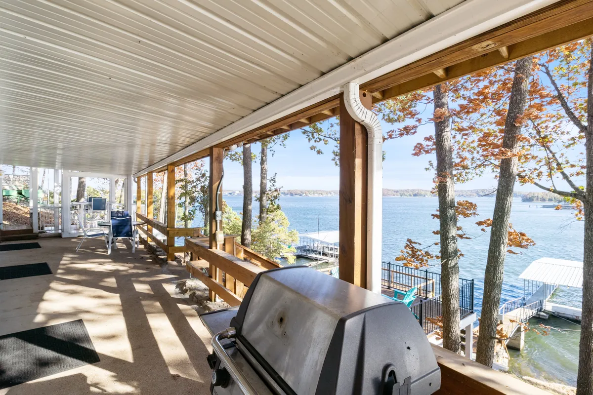 An outdoor setup featuring a grill, trees, and a dock extending into the lake. The water view is inviting, and the dock is visible, suggesting easy access and a setting for lakeside activities and socializing.