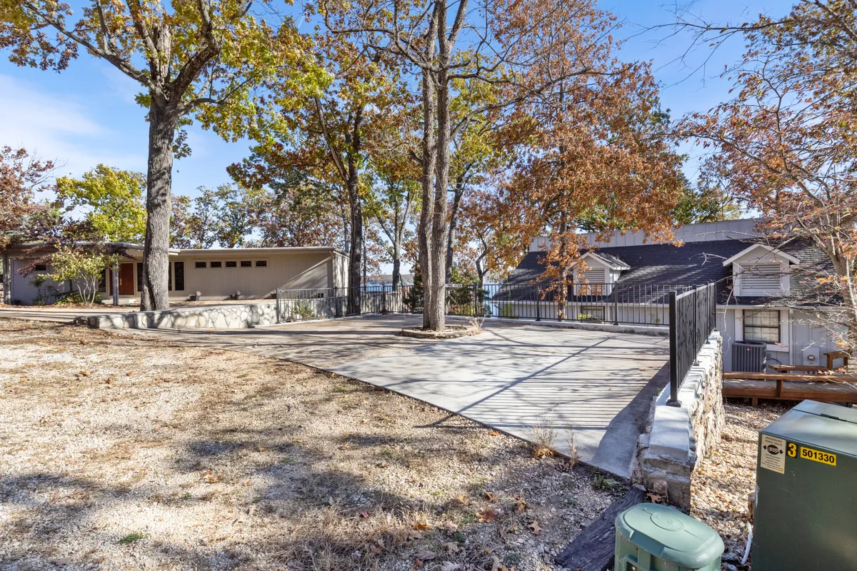 This image showcases a spacious patio shaded by large trees, with an inviting water view in the background. The scene evokes relaxation and social interaction, ideal for outdoor gatherings, barbecues, or simply enjoying the tranquil lakeside setting with friends and family.