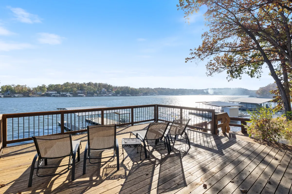 A wooden deck overlooking the tranquil lake, featuring outdoor seating ideal for relaxing. The view includes lush greenery, calm water, and an open sky, inviting guests to unwind and take in the peaceful setting.