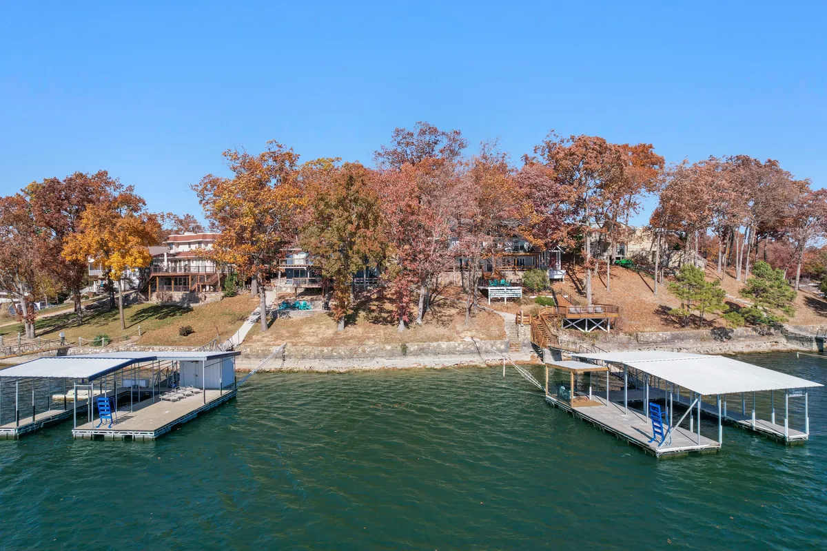 A tranquil lakeside vista showcasing colorful autumn trees, waterfront docks, and the property structure. The calm water reflects the vibrant foliage, suggesting opportunities for boating, fishing, and soaking in the seasonal beauty.
