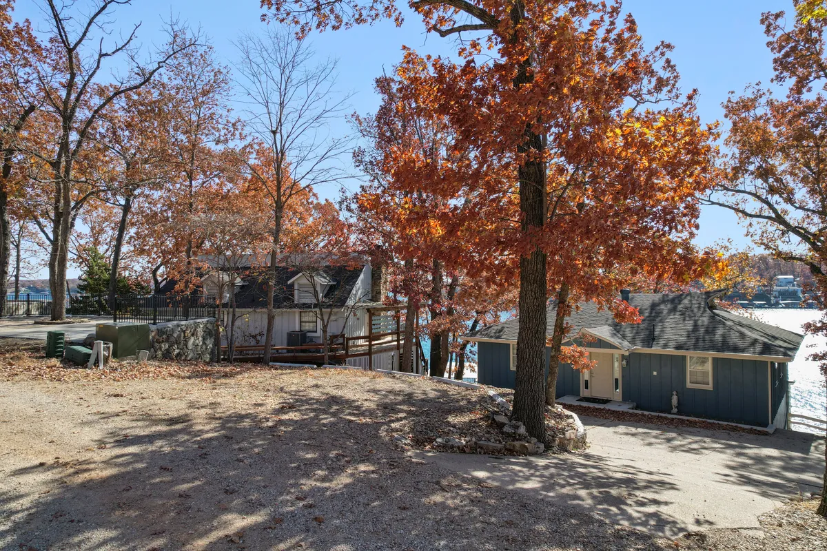 This exterior shot features vibrant autumn foliage framing two distinct houses with a beautiful water view beyond. The setting is cozy yet expansive, suggesting space for family gatherings, outdoor activities, and lakeside fun.