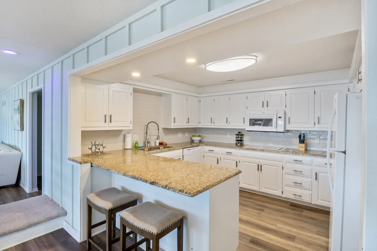 A modern kitchen scene featuring a gleaming granite countertop, white cabinetry, and bar stools, inviting cooking, conversation, and casual dining. The cheerful, welcoming atmosphere encourages sociability and participation in meal prep.